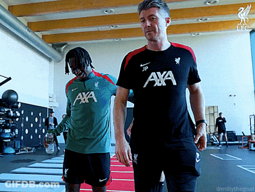 Man In Aya Shirt Walking Next To Man In Green Shirt GIF