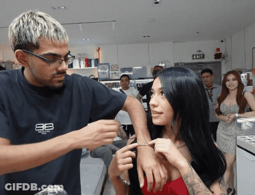 Man In Balenciaga Shirt Adjusting Woman's Wrist GIF