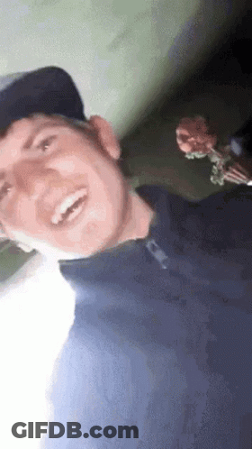 Man In Baseball Cap Blue Shirt Smiling Holding Flower GIF