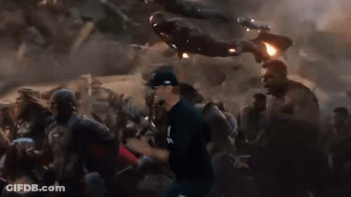 Man In Baseball Cap Running Through Crowd While Iron Man Flies Overhead GIF