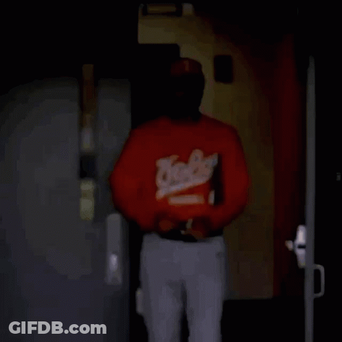 Man In Baseball Jersey And Sunglasses Walking Through Dark Room GIF