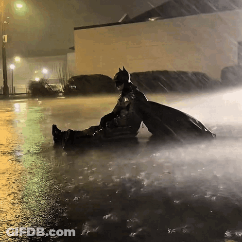 Man In Batman Costume Laying In Rain GIF