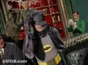 Man In Batman Costume Standing In Front Of TV Sign GIF