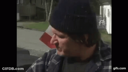 Man In Beanie And Plaid Shirt Sitting In Front Of Flag GIF