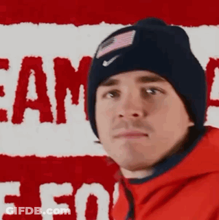 Man In Beanie And Red Jacket In Front Of Flag GIF