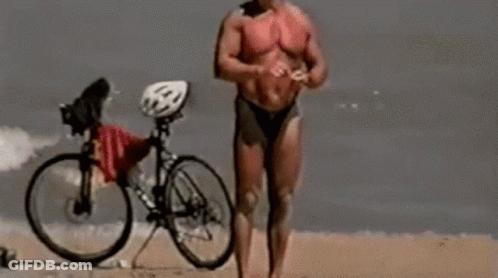 Man In Bikini Standing On Beach With Bike GIF