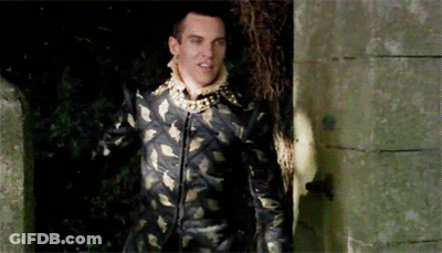 Man In Black And Gold Suit Standing Before Stone Wall GIF