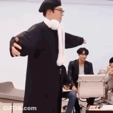 Man In Black Coat And White Scarf Standing In Front Of Group GIF