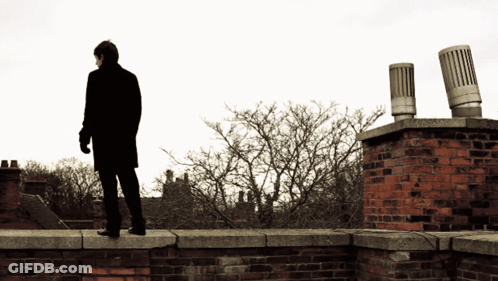Man In Black Coat Standing On Brick Wall GIF