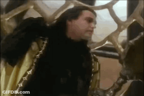 Man In Black Fur Coat Standing Next To Snake Statue GIF