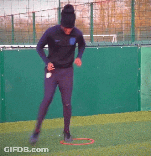 Man In Black Hat Jumping Through Red Hoop On Soccer Field GIF
