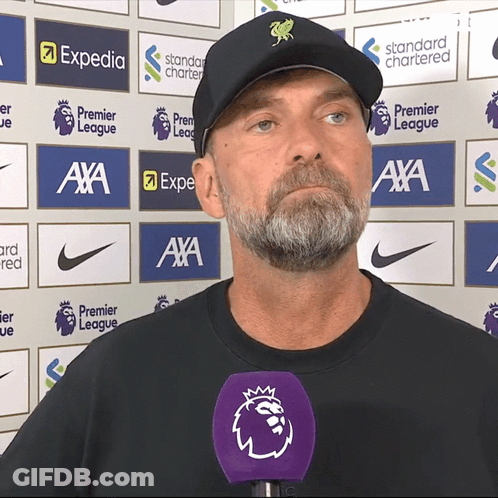Man In Black Hat With Purple Mic In Front Of Expedia And Standard Chartered Logos GIF