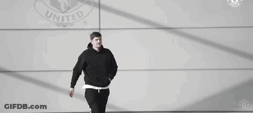 Man In Black Hoodie And Pants Walking In Front Of United Logo Wall GIF