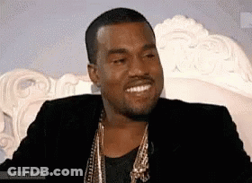 Man In Black Jacket And Gold Chains Smiling On Couch GIF