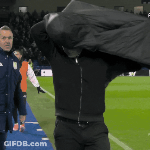 Man In Black Jacket Holding Bag Over Head On Soccer Field GIF