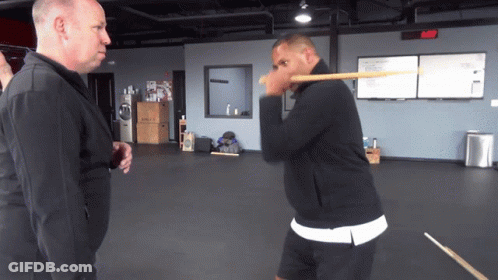 Man In Black Jacket Holding Stick To Face GIF
