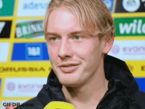 Man In Black Jacket In Front Of Yellow Wild Sign GIF