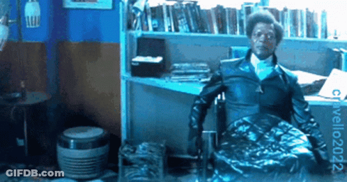 Man In Black Jacket Sitting By Bookshelf GIF