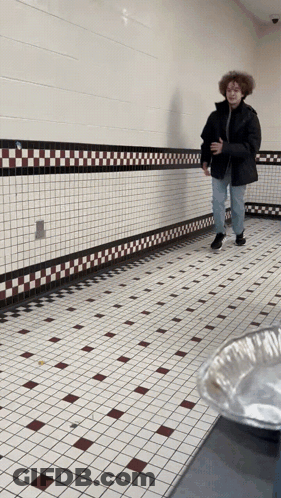 Man In Black Jacket Walking Down Tiled Hallway GIF