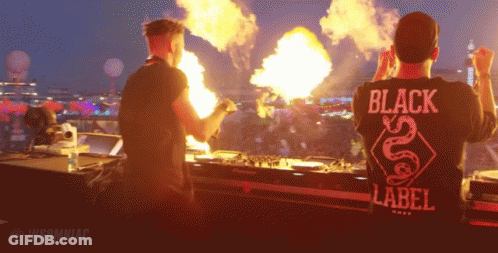 Man In Black Label Shirt In Front Of Fire GIF