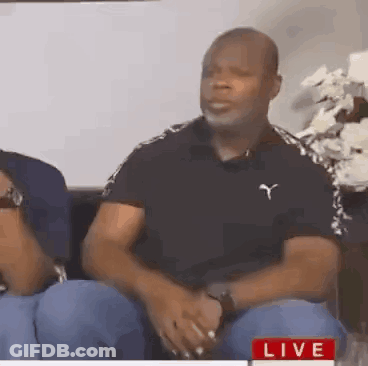 Man In Black Puma Shirt Sitting On Couch Talking To Another Man GIF