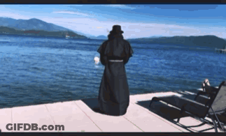 Man In Black Robe On Dock Overlooking Lake GIF