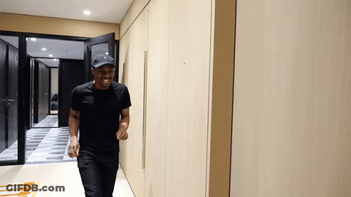 Man In Black Shirt And Baseball Cap Walking Down Hallway GIF