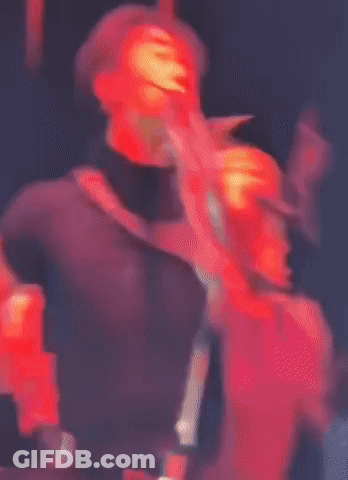 Man In Black Shirt And Pants Cross-Legged On Stage GIF