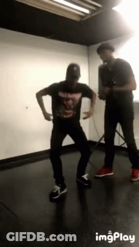 Man In Black Shirt Dancing Behind Man With Camera GIF
