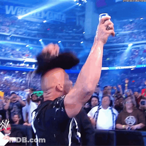 Man In Black Shirt Holding Can In Front Of Wrestlemania Sign GIF