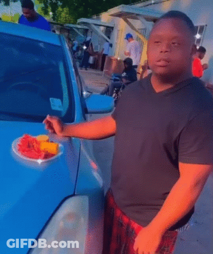 Man In Black Shirt Holding Plate Of Fruit In Front Of Car GIF