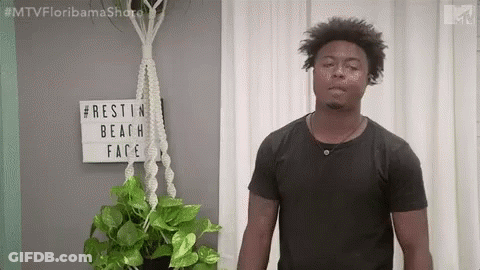 Man In Black Shirt Next To Potted Plant And Rest In Beach Face Sign GIF