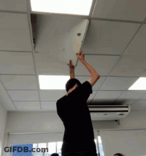 Man In Black Shirt Reaching Up To Remove Paper From Ceiling GIF