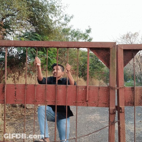 Man In Black Shirt Sitting Behind Red Gate GIF