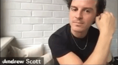 Man In Black Shirt Sitting By Brick Wall Hand On Ear GIF