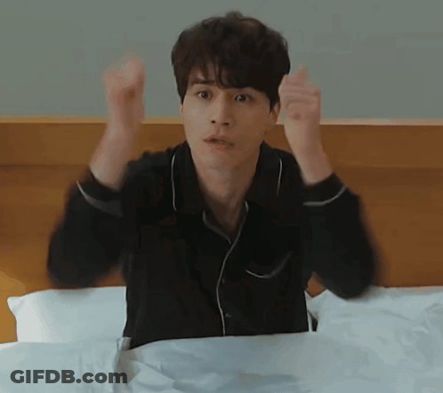 Man In Black Shirt Sitting On Bed With Arms In Air GIF