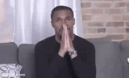 Man In Black Shirt Sitting On Couch With Hands Folded In Prayer GIF
