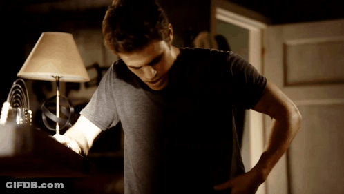 Man In Black Shirt Standing Before Lamp In Dark Room GIF