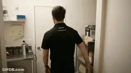 Man In Black Shirt Standing In Room With Shelf GIF