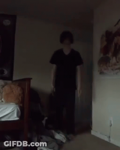 Man In Black Shirt Standing Next To Bed In Dark Room GIF