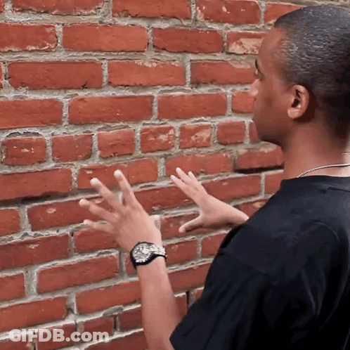 Man In Black Shirt Touching Brick Wall GIF