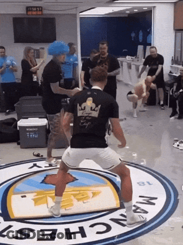 Man In Black Shirt With Crown Dancing In Front Of Manchester Logo GIF
