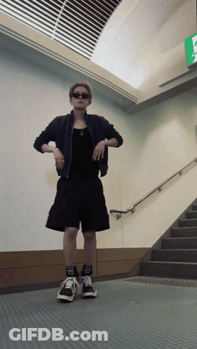 Man In Black Shorts And Jacket In Front Of Staircase GIF