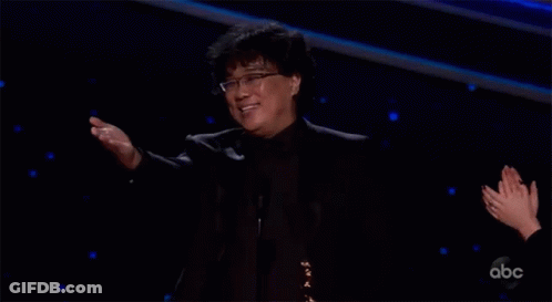 Man In Black Suit And Glasses Arms Outstretched On Stage GIF