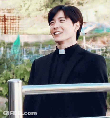 Man In Black Suit And Priest Collar Smiling Beside Fence GIF