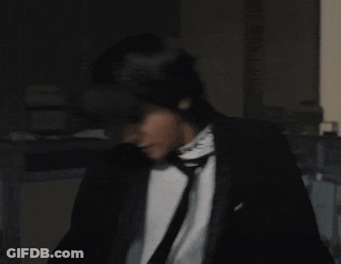 Man In Black Suit And Tie With Green Necklace GIF
