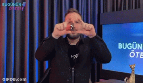 Man In Black Suit Making Hand Gesture In Front Of Bugun Screen GIF