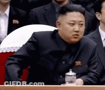 Man In Black Suit Sitting Before Group Of Men GIF