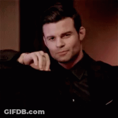 Man In Black Suit Sitting With Hand On Shoulder GIF