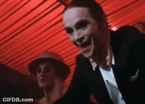 Man In Black Suit Smiling Before Red Canopy GIF